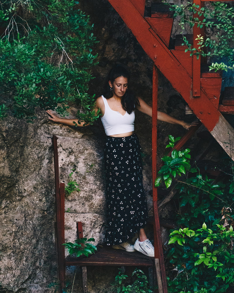Close up view of woman in white shirt and black skirt standing on red stairs looking into a cenote in Mexico